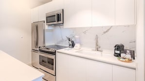 Una cucina moderna con elettrodomestici in acciaio inossidabile, una parete di fondo in marmo e una macchina da caffè sul piano di lavoro.