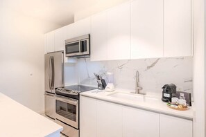 Eine moderne Küche mit Edelstahlgeräten, einer Marmor-Spritzschutzwand und einer Kaffeemaschine auf der Arbeitsfläche.