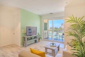 Ein Wohnzimmer mit Fernseher, einer Couch, einem Couchtisch und einem Balkon mit Gartenmöbeln.