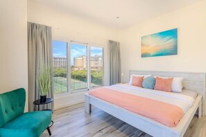 Habitación de hotel con una cama grande, un sillón verde, una mesita con una planta y un cuadro en la pared.