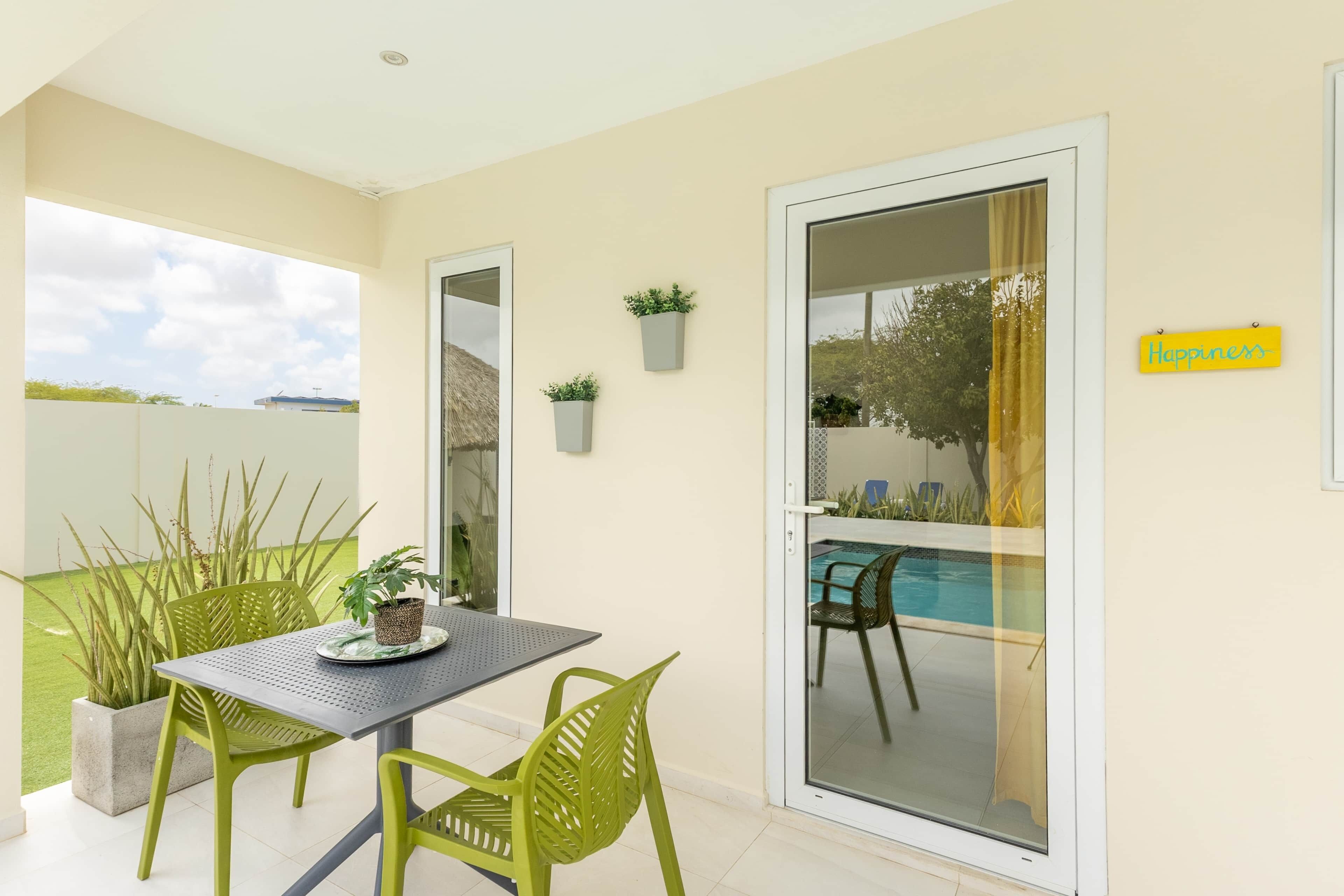 Une terrasse avec une table et des chaises, une porte-fenêtre coulissante donnant sur une piscine et un panneau mural portant l’inscription « Bonheur ».