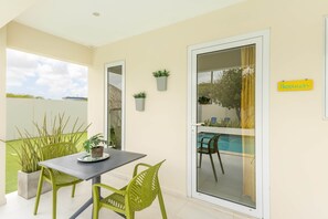 Une terrasse avec une table et des chaises, une porte-fenêtre coulissante donnant sur une piscine et un panneau mural portant l’inscription « Bonheur ».
