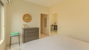 A bedroom with a bed, a dresser, a stool, a wall-mounted decorative item, and a doorway leading to a bathroom.
