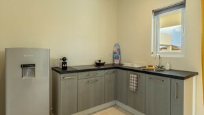 A compact kitchen with grey cabinets, a built-in fridge, a window with a view, and a small countertop.