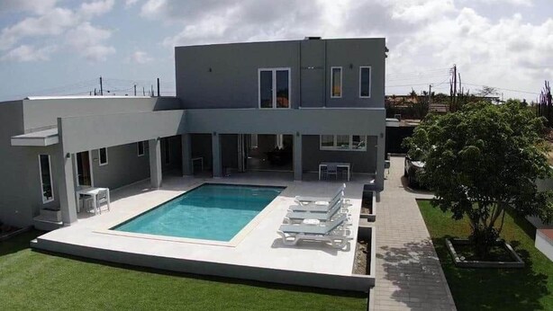 A modern two-story house with a swimming pool, a patio with lounge chairs, and a well-maintained lawn.