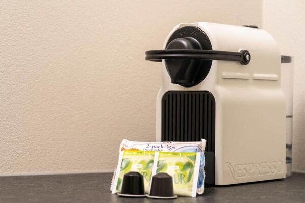 Uma máquina Nespresso branca com duas cápsulas de café e duas xícaras em frente a ela.