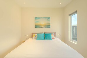 Une chambre avec un grand lit, un tableau représentant un coucher de soleil et une fenêtre donnant sur un beau paysage.