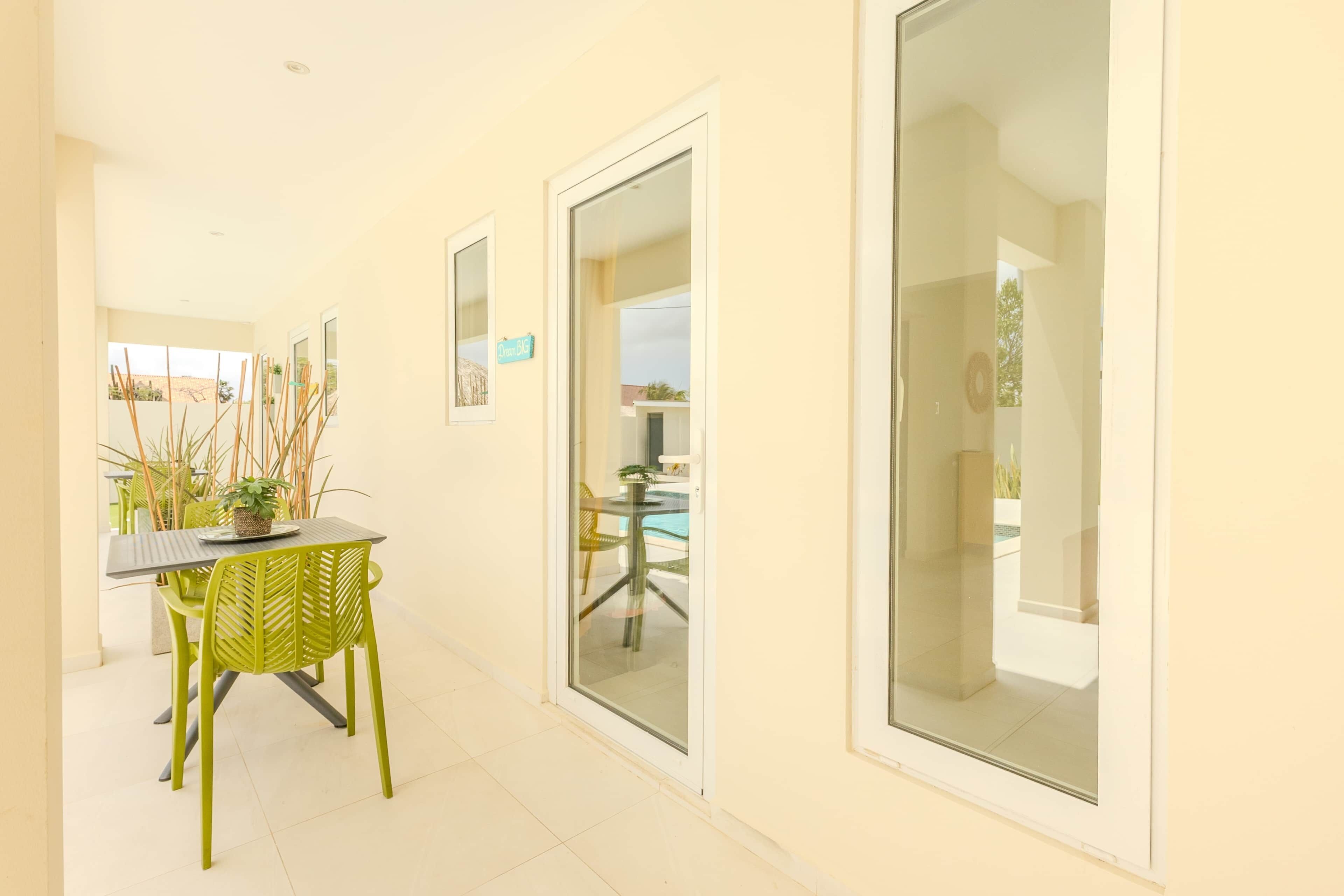Un couloir qui mène à un coin repas, comprenant une table et des chaises, une plante en pot, et une vue sur un espace extérieur avec piscine, visible à travers une porte vitrée.