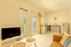 A living room with a flat-screen TV, a small table, a sofa, and a kitchen area with a refrigerator, stove, and sink. - Hideout Dream Big Suite- From Eagle Beach (Noord)