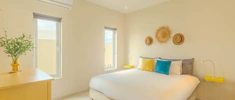 Quarto com cama, mesas de cabeceira, uma planta em vaso e uma janela.