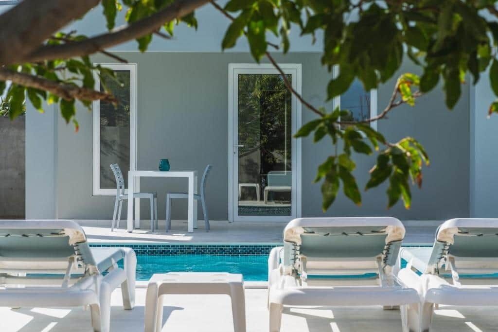 Un espace piscine avec des chaises longues, une table et des chaises, ainsi qu’un bâtiment doté de grandes fenêtres.