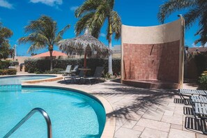 Ein Pool mit Liegestühlen, einem schattigen Bereich und Palmen.