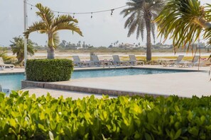 A pool area with lounge chairs, palm trees, and a hedge. - Gated Gold Coast 1BR, 75 m², 3 pools, near Malmok (Noord)