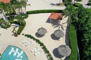 Un complejo turístico en la playa con piscina, sillas de descanso y sombrillas de techo de paja.