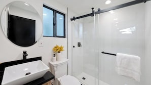 Un baño moderno con lavamanos blanco, espejo y cabina de ducha con vidrio.