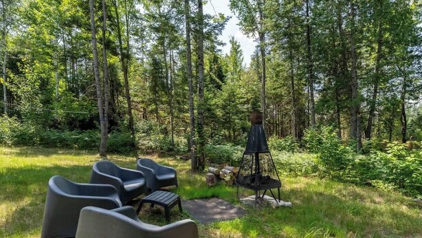 A forested area with outdoor seating, a fire pit, and a table. - Le Clorane | spa | relax (Matawinie Regional County Municipality)