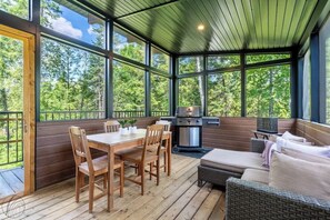 Ein überdachter Außenbereich mit Holztisch und -stühlen, einem Grill und einer Couch.