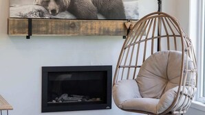 A living room with a black sofa, a hanging chair, a fireplace, and a bear photograph on the wall. - Le Clorane | spa | relax (Matawinie Regional County Municipality)
