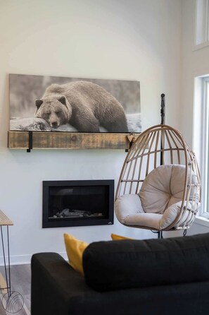 Ein Wohnzimmer mit schwarzem Sofa, einem Hängesessel, einem Kamin und einem Bärenfoto an der Wand.