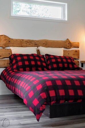 A bed with a wooden headboard, a checkered bedspread, and white pillows. - Le Clorane | spa | relax (Matawinie Regional County Municipality)