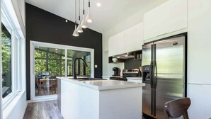 A modern kitchen with a central island, stainless steel appliances, and a large window overlooking greenery. - Le Clorane | spa | relax (Matawinie Regional County Municipality)