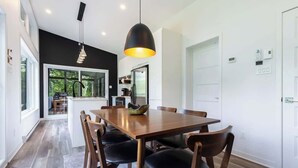 A modern dining area with a wooden table and chairs, a pendant light, and a view of the kitchen through a glass door. - Le Clorane | spa | relax (Matawinie Regional County Municipality)