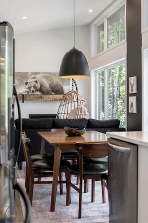 A modern dining area with a wooden table, black leather chairs, a hanging pendant light, and a wall-mounted picture of a bear. - Le Clorane | spa | relax (Matawinie Regional County Municipality)