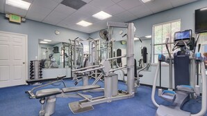 Ein Fitnessraum mit Trainingsgeräten, einem Spiegel, einer Uhr und einem Ausgangsschild.