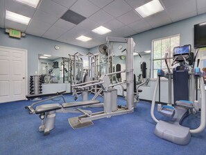 Ein Fitnessraum mit Trainingsgeräten, einem Spiegel, einer Uhr und einem Ausgangsschild.