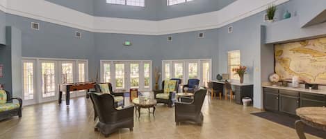 A spacious lobby with high ceilings, multiple seating areas, a pool table, and a map on the wall.