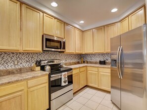 A kitchen with wooden cabinets, a stainless steel refrigerator, a microwave, an oven, and a herringbone-patterned backsplash. - Amazing 2-bedroom condo in peaceful Kissimmee with AC and gym (Kissimmee)