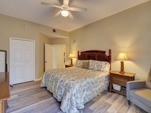 A bedroom with a bed, two bedside tables with lamps, a chair, a ceiling fan, and a door. - Amazing 2-bedroom condo in peaceful Kissimmee with AC and gym (Kissimmee)