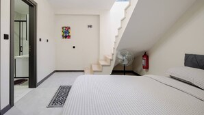 Een slaapkamer met een bed, een ventilator, een brandblusser en een trap.