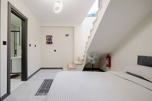 Ein Schlafzimmer mit einem Bett, einem Standventilator, einem Feuerlöscher und einer Treppe.