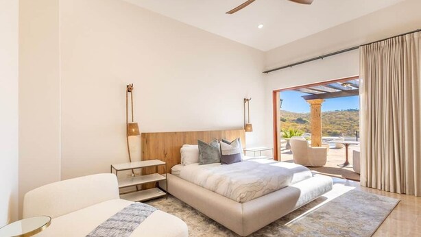 Ein Schlafzimmer mit einem Bett, einem Sessel, einem kleinen Tisch, einem Deckenventilator und Blick ins Freie.
