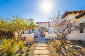 A courtyard with a stone pathway leading to a building with a tiled roof and a door. - Luxury Mediterranean Villa in Querencia (San José del Cabo)