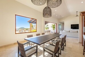 Un espace repas comprenant une longue table et des chaises, une grande fenêtre offrant une belle vue et un luminaire moderne au plafond.