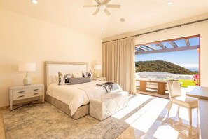 Une chambre à coucher avec un lit, des tables de chevet, un bureau et une vue sur une colline.