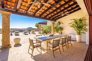 An outdoor patio with a table and chairs, potted plants, and a view of the landscape. - Luxury Mediterranean Villa in Querencia (San José del Cabo)