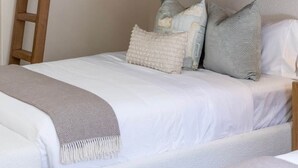 Ein Stockbett mit Holzleiter, weißer Bettwäsche und vielen Kissen.