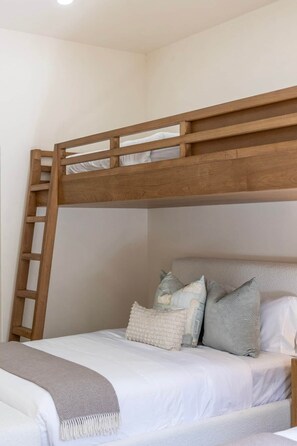 Ein Stockbett mit Holzleiter, weißer Bettwäsche und vielen Kissen.