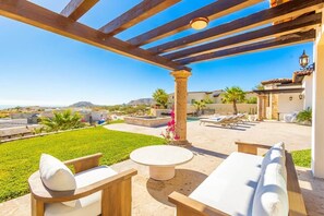A covered outdoor seating area with a pool, lounge chairs, and a view of the landscape. - Luxury Mediterranean Villa in Querencia (San José del Cabo)
