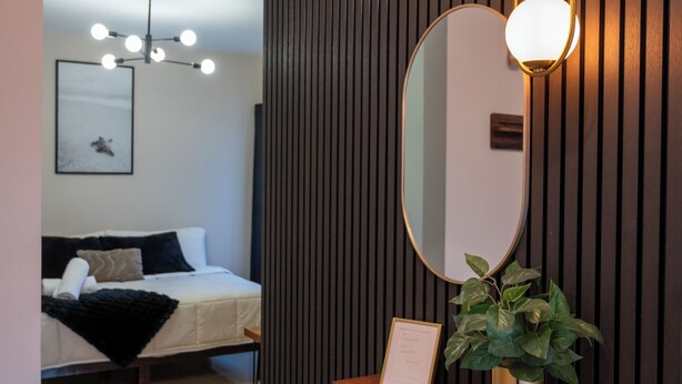 Una moderna camera d'albergo con un letto, un comodino con una pianta, uno specchio a parete e una lampada a soffitto.