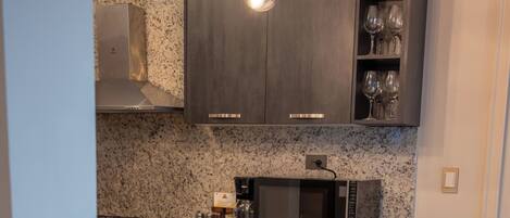 A kitchen with granite countertops, a stainless steel range hood, a microwave, and a bar area with black velvet bar stools and gold legs.