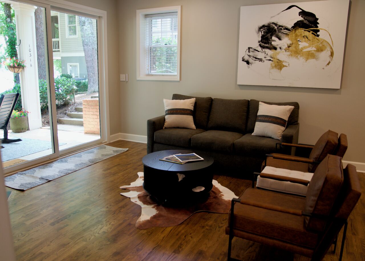 A living room with a sofa, armchairs, a coffee table, and a large abstract painting on the wall.