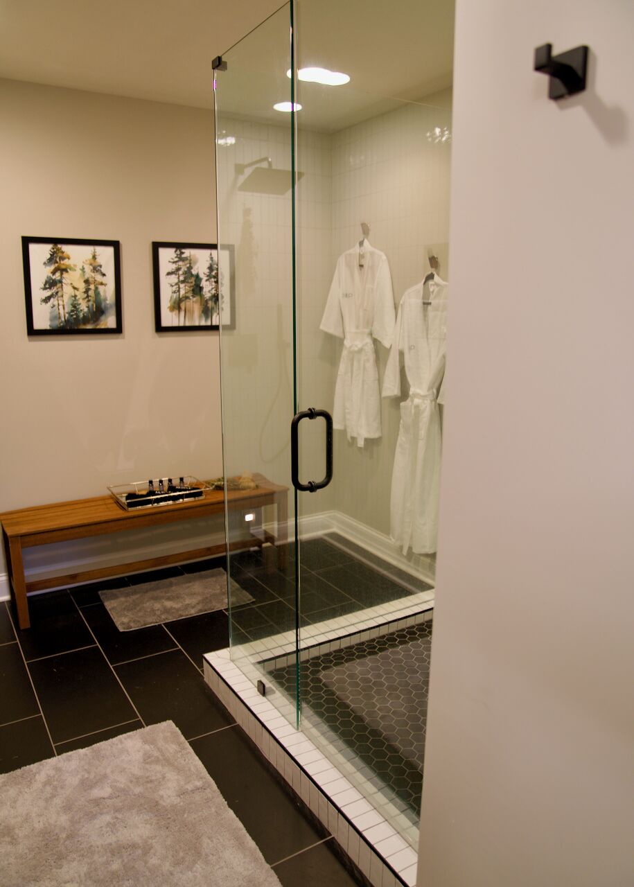 Une salle de bain moderne avec une douche à parois de verre, un banc en bois et deux tableaux encadrés au mur.