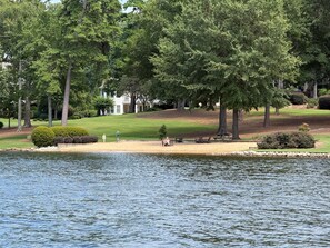 A lakeside view with a grassy area, trees, and a building in the background.