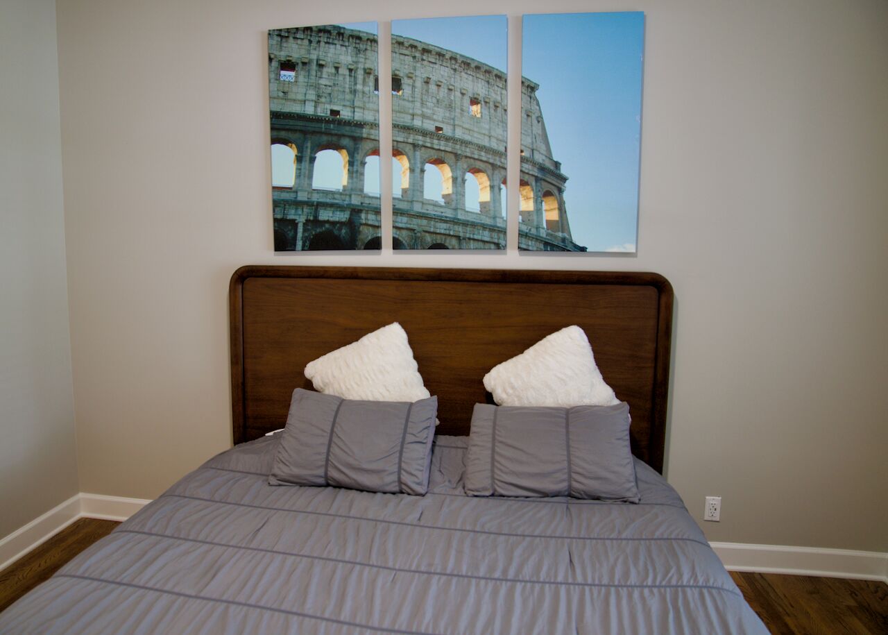 Une chambre à coucher avec un lit, des oreillers et un tableau représentant le Colisée, accroché au mur.