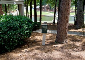 A signpost with the text '1031B Marina Cove Lane (downstairs)' in a landscaped area with trees and a grassy background.