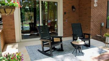 A patio with two rocking chairs and a small table, a brick wall, and a sliding glass door leading to an outdoor area.